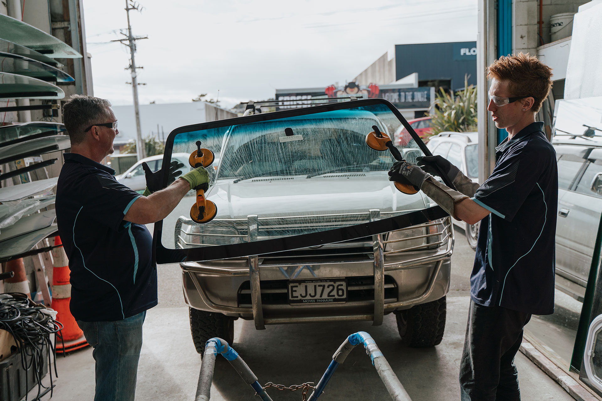 Two technicians lifting a new windscreen into place